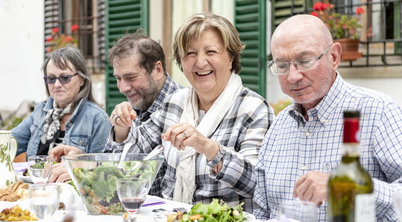 A group of four older people sat in a row while eating salad outdoors