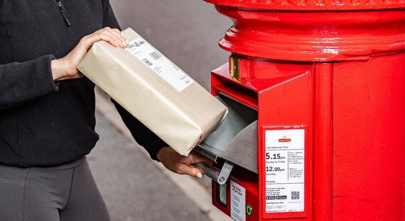 Close up of a person putting a parcel into the slot of a new postbox