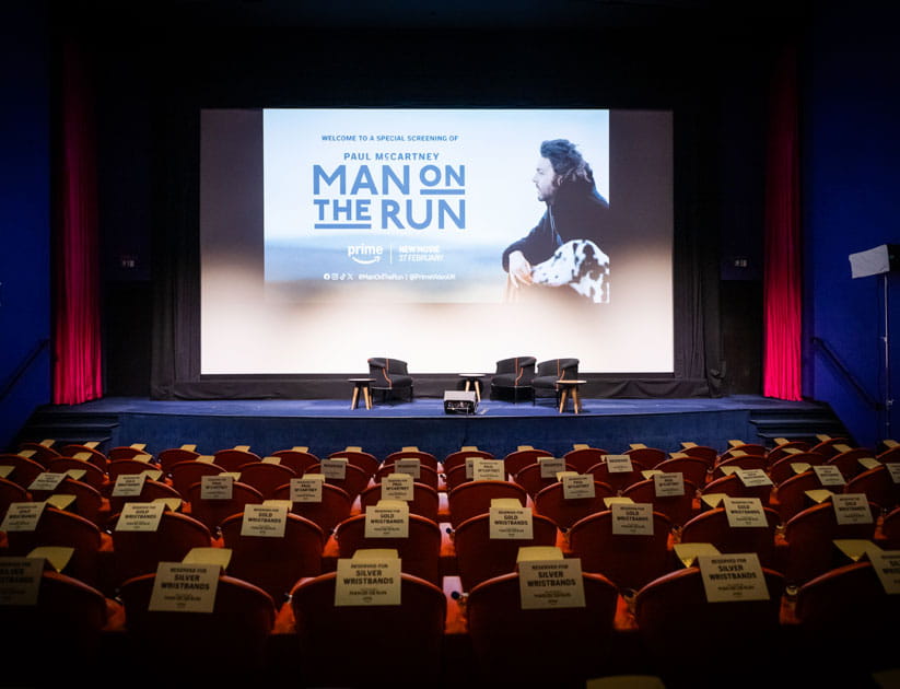 Theatre with chairs facing a stage with a big screen displaying man on the run