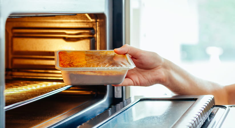 Close up of a hand putting a ready meal into a microwave oven