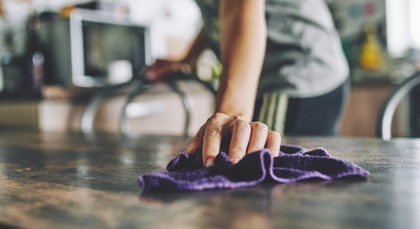 Close up of a female in a grey top cleaning a kitchen work surface with a cloth