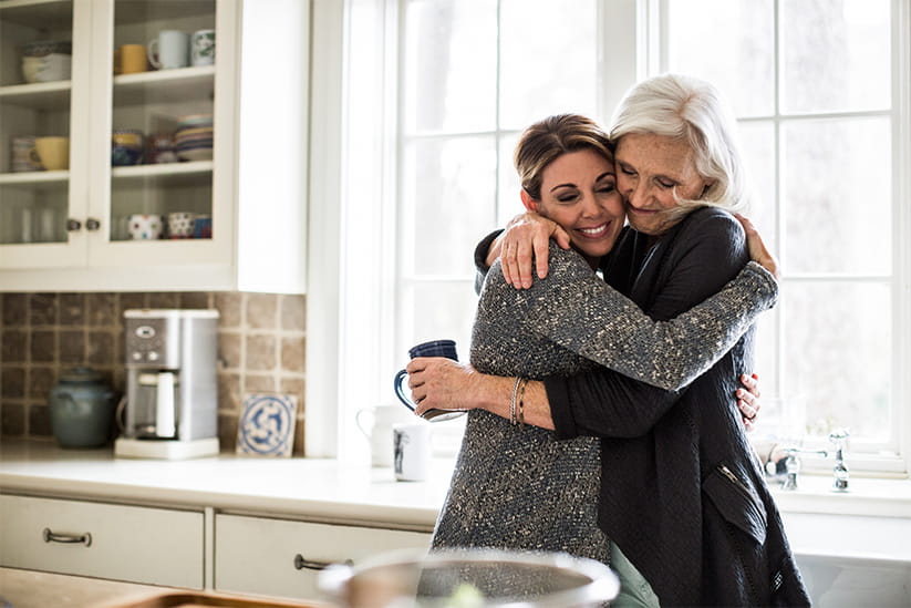 Mother and adult daughter hugging in kitchen