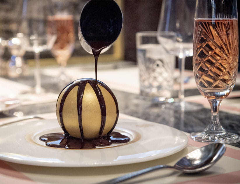 A decadent dessert which looks like a golden globe with chocolate being poured over it