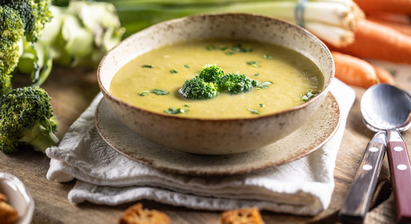 Close up of a bowl of broccoli soup on a table with some cutlery
