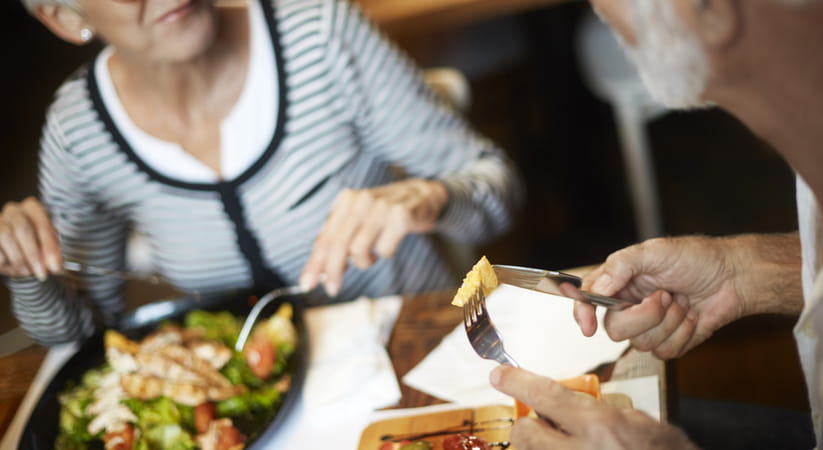 Close up of an older couple eating salad at a table