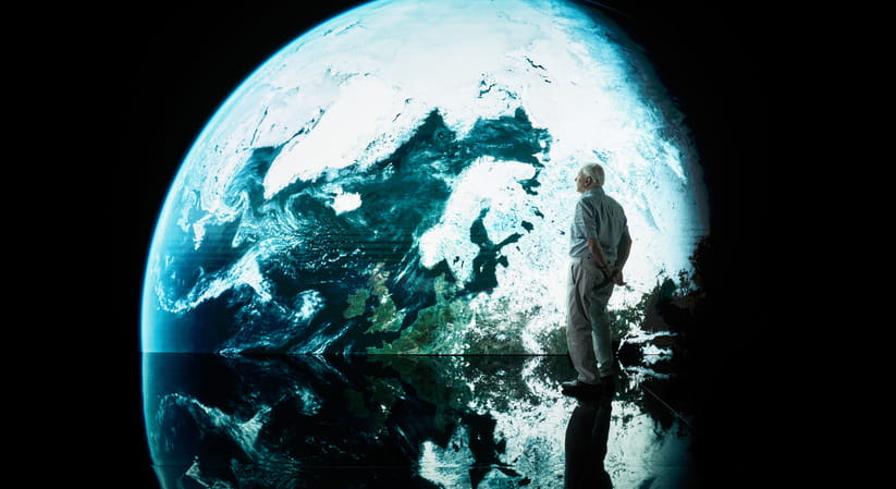 David Attenborough stands next to a large projection of the planet Earth