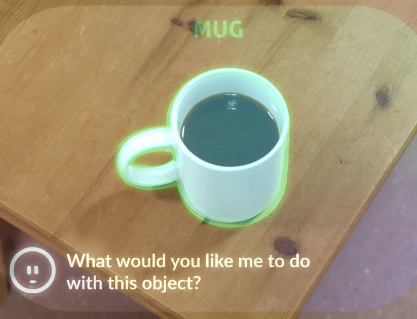 A user's view through CrossSense AI dementia glasses of a a mug on a table with text from the Wispy assistant reading: Mug what would you like me to do with this object