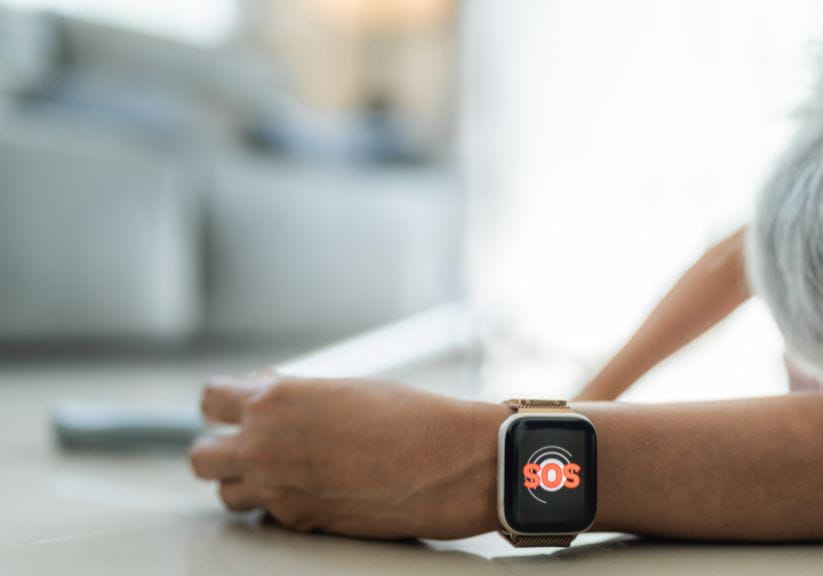 A lady lies on the ground while her smart watch sends an alert, SOS is seen on her watch face