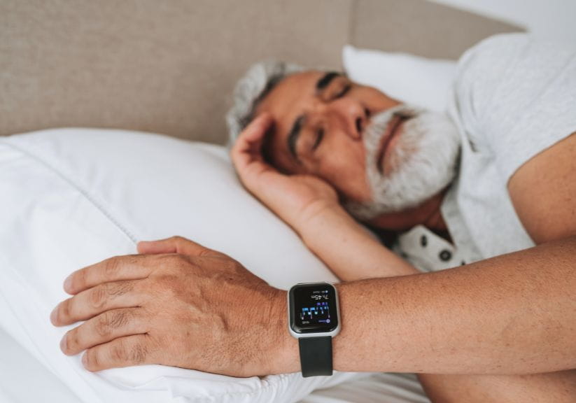 A mature man lies in bed with a fitness tracker on his wrist