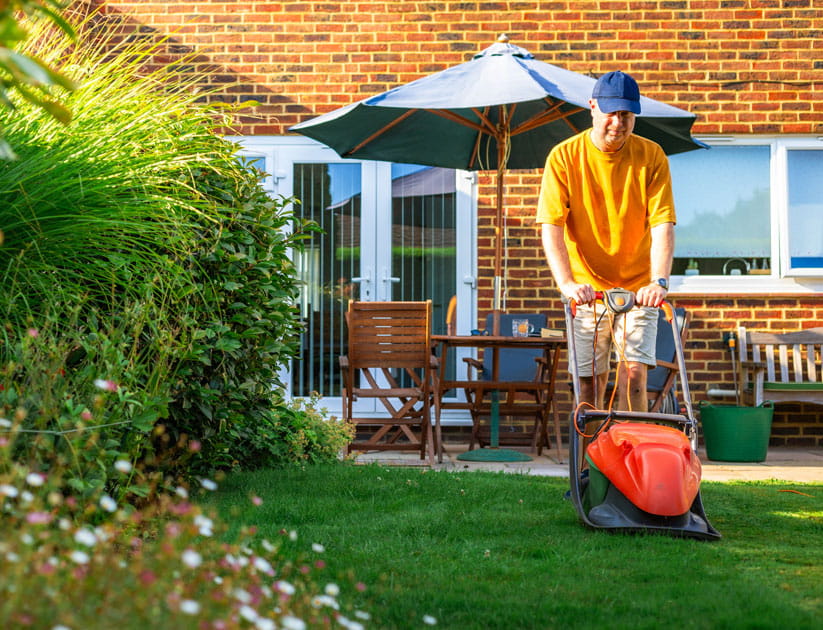 A man mowing the lawn with an electric lawn mower on a sunny summer evening