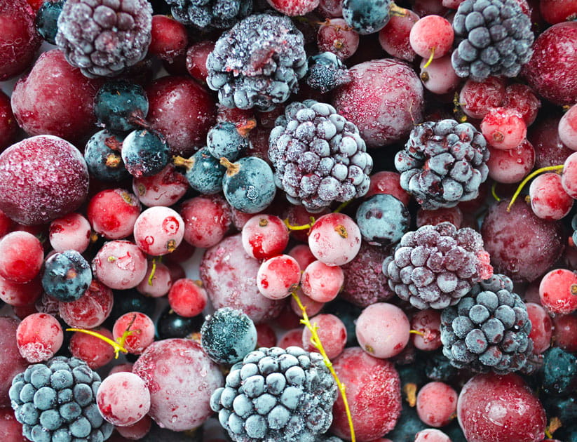 A vibrant assortment of frozen berries, including blackberries, red currants, cherries, and blue currants, covered in frost