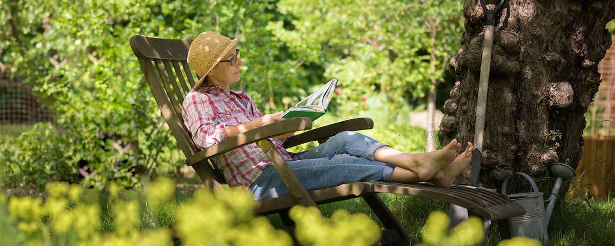 An older woman sitting in a deck chair in her garden reading a book