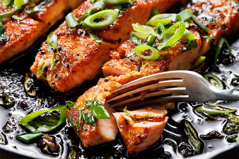 Close-up view of teriyaki salmon sprinkled with chopped scallion on a black background