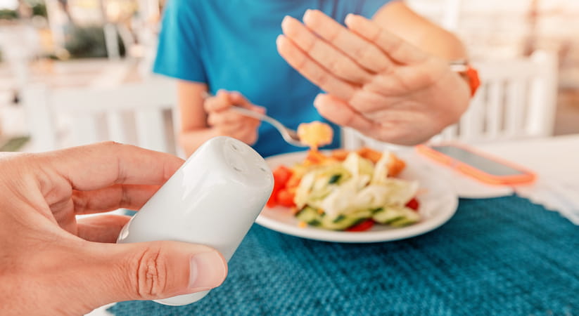 Close up of a woman in a blue top raising her hand to turn away a salt pot