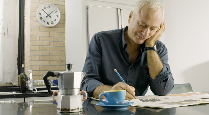 An older man in a dark shirt sits at the kitchen table doing a puzzle