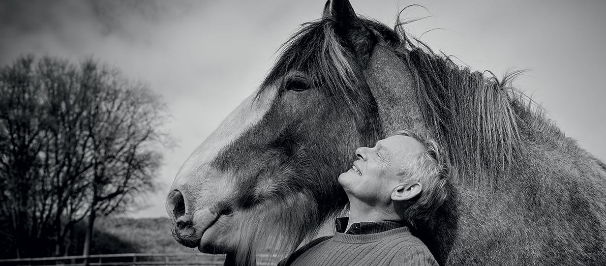 Black and white image of actor Martin Clunes posing with a horse