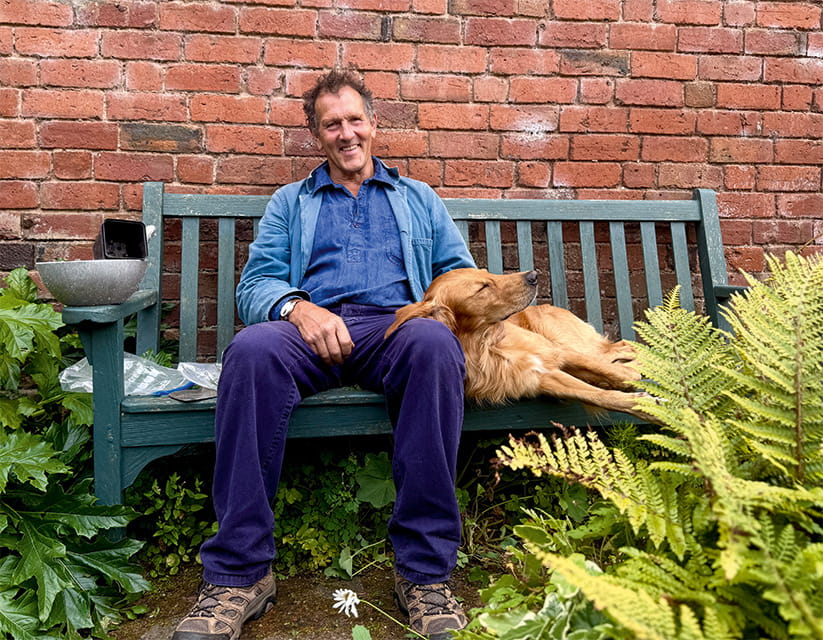 Monty Don sitting on a garden bench with a dog
