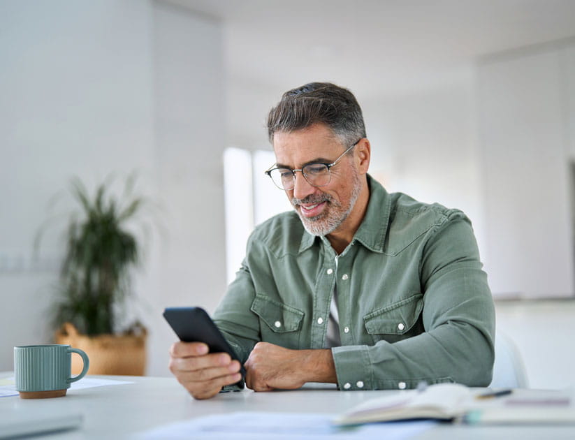  Mature man using mobile phone sitting at kitchen table