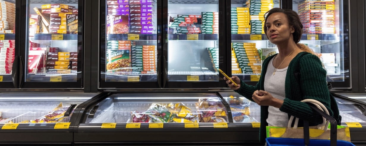 A woman looking at food at a supermarket freezer cabinet