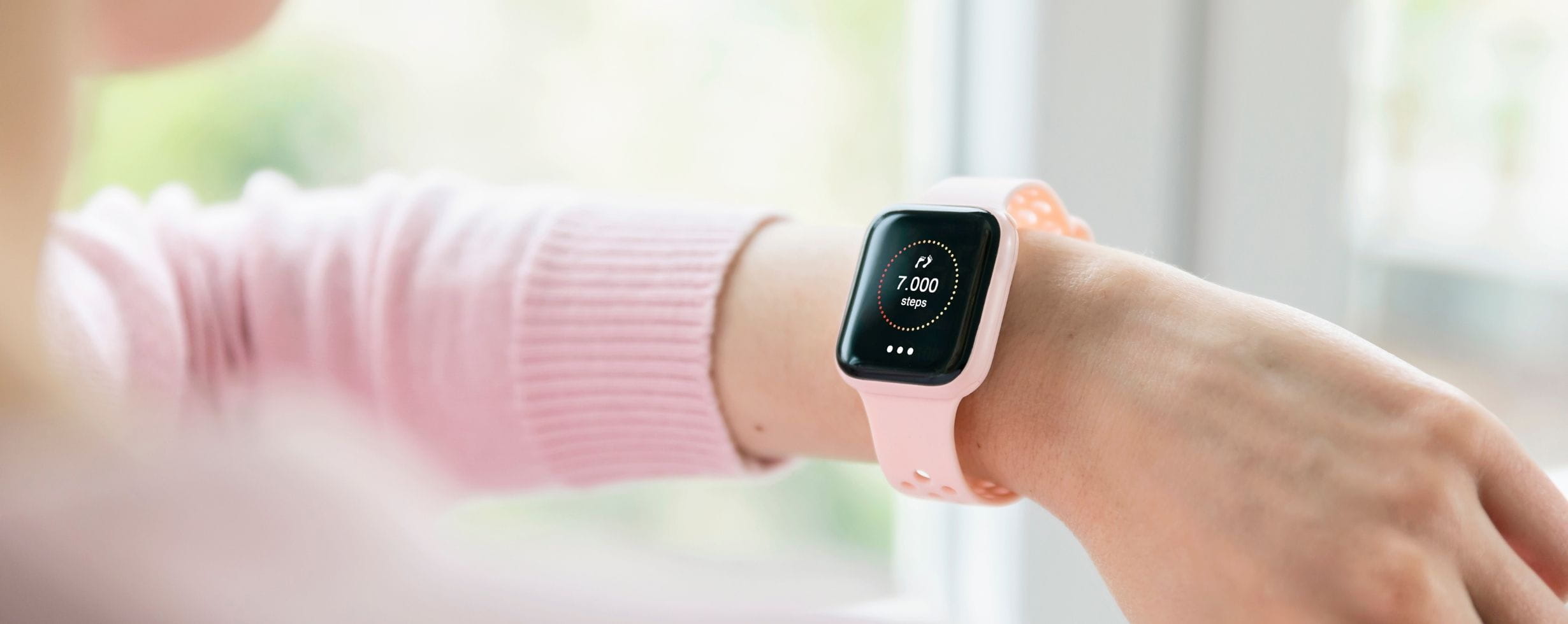 A woman's with a fitness tracker on her wrist. She is turning her wrist as if to look at it but only a tiny piece of her head is in the shot