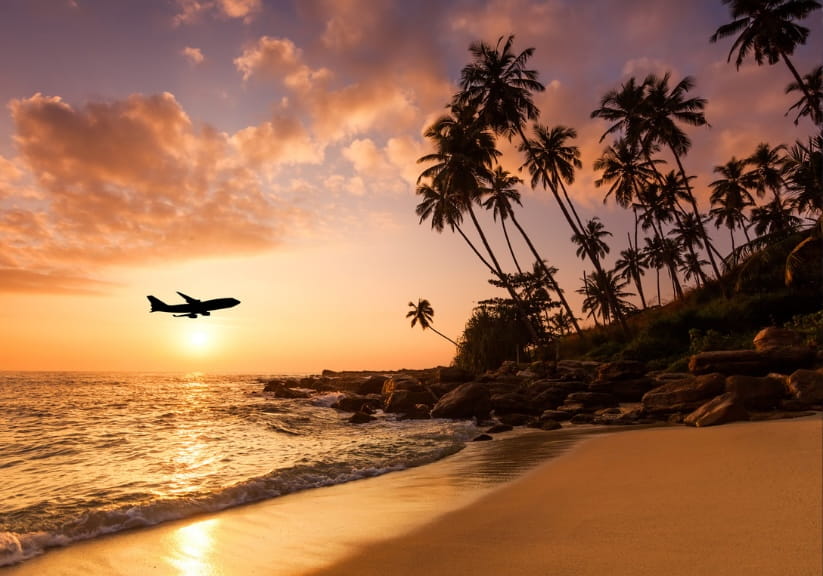 A plane flying low over a tropical island at sunset