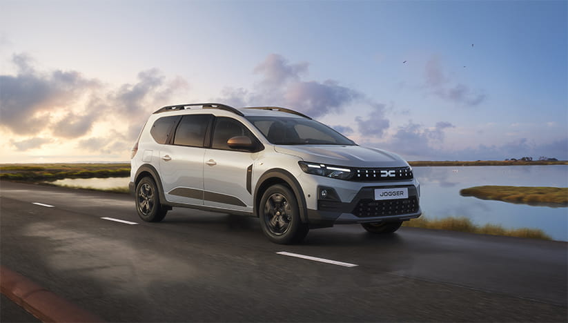 A silver Dacia Jogger Extreme driving along a lakefront
