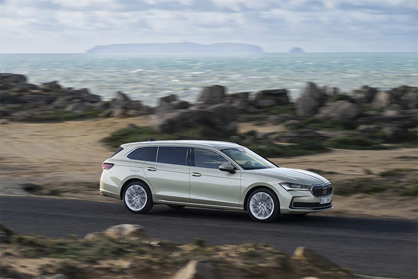 A silver Skoda Superb Estate driving on a road past a rocky seafront