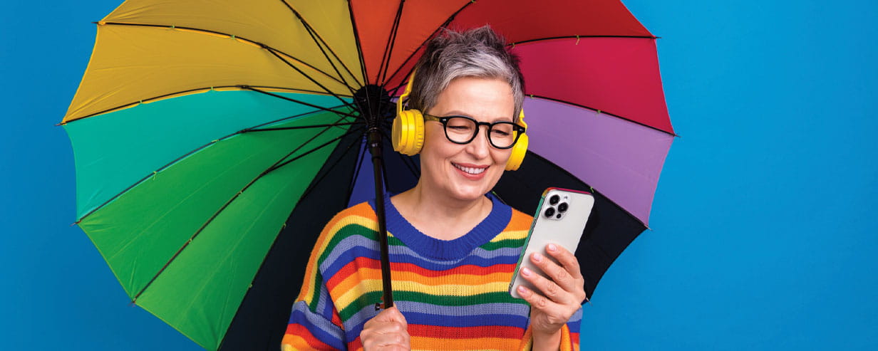 Photo of charming cheerful aged lady hold umbrella using a mobile phone isolated on blue color background.
