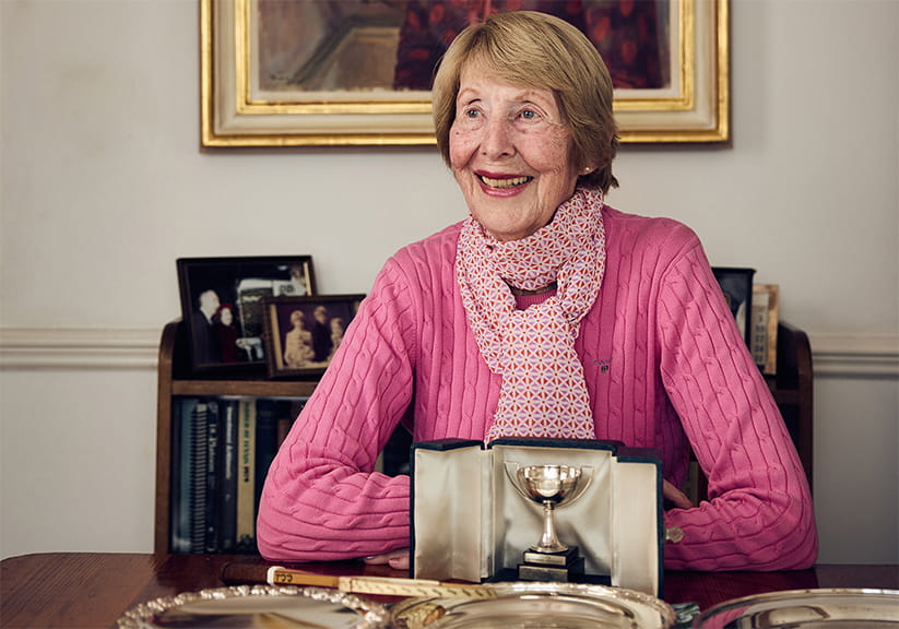 Christine sitting at a table with her tennis trophies