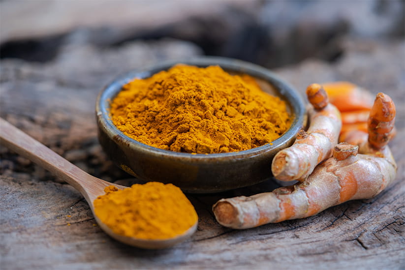 Turmeric powder and fresh turmeric in wood bowls on wooden table