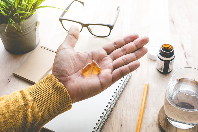 An older man holding two omega-3 supplements in his hand