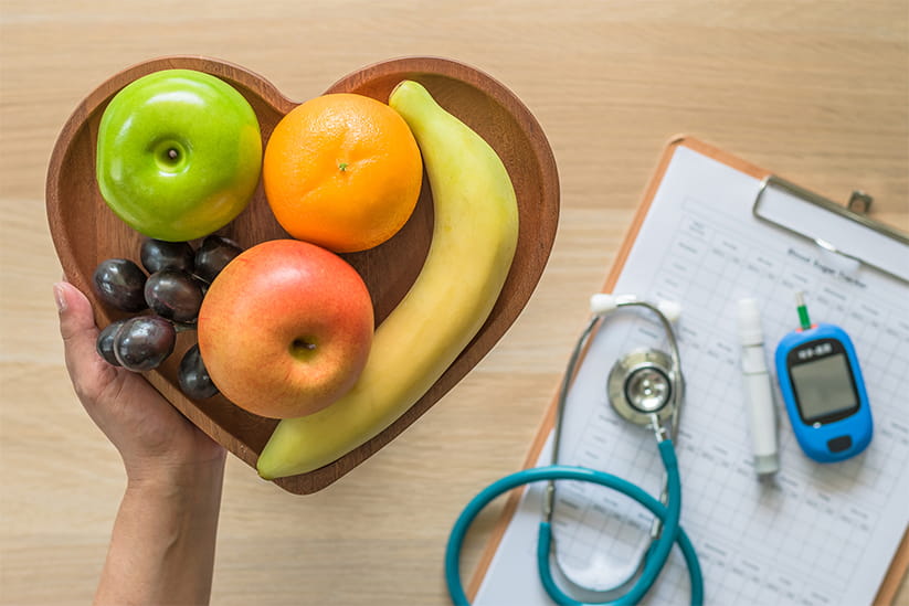 Fruit in a hear shaped bowl being held by a doctor over a table with health-monitoring equipment on it 