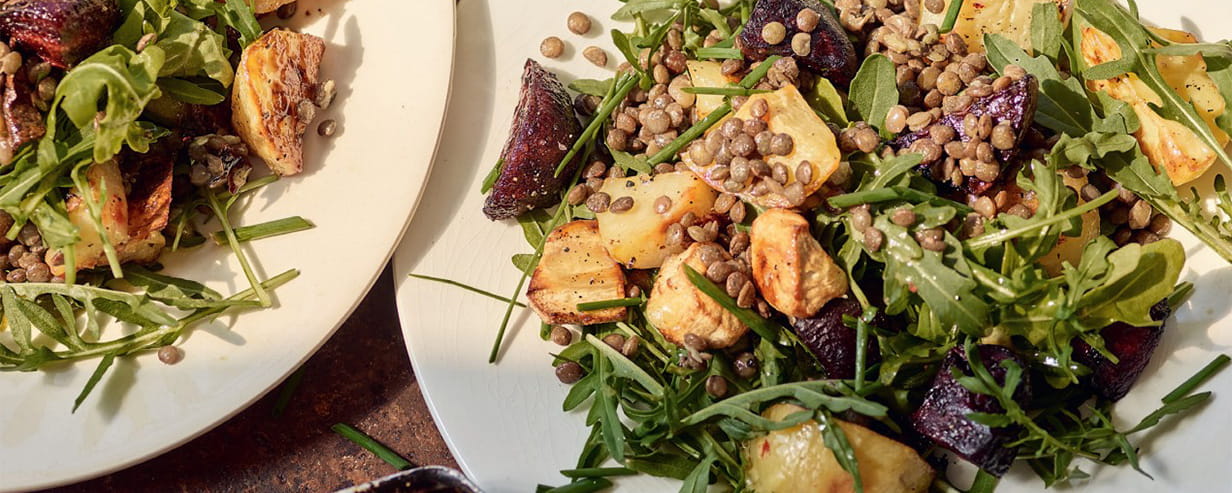 Roasted root and lentil salad on white plates on a rustic wooden table