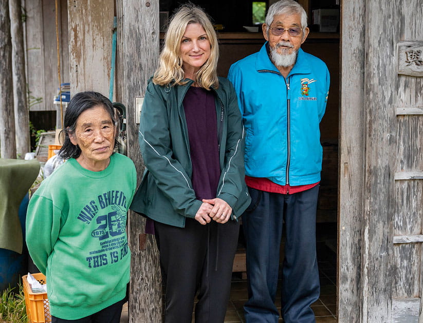 Kirsty Tyler standing with Etsuko (left) and Rikio (right) at the doorway to their home in the village of Higashi in north Okinawa