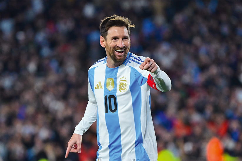 Lionel Messi in his national kit smiling and pointing at the crowd
