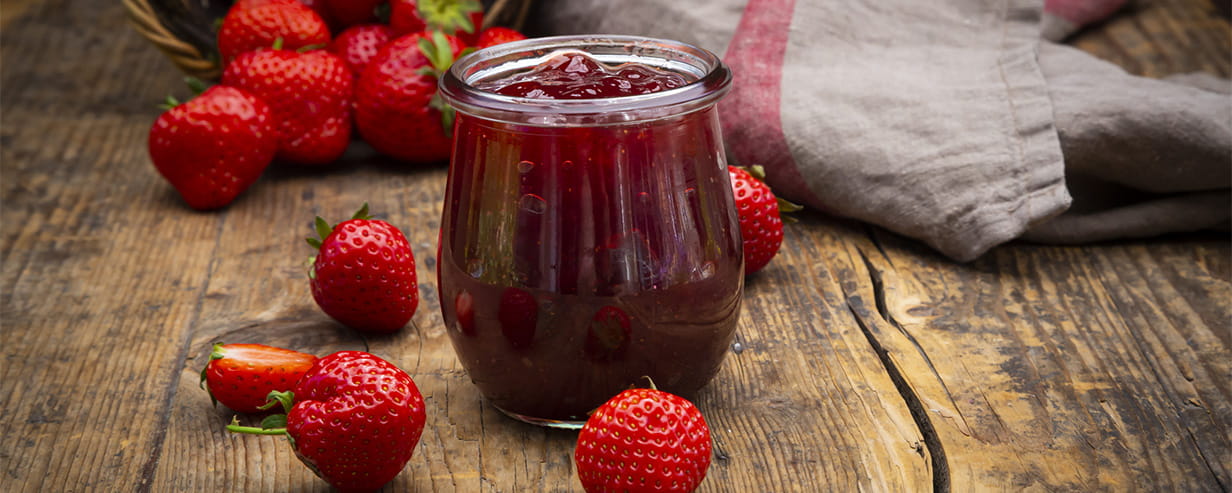 Glass of homemade strawberry jam on a dark wood table with fresh strawberries