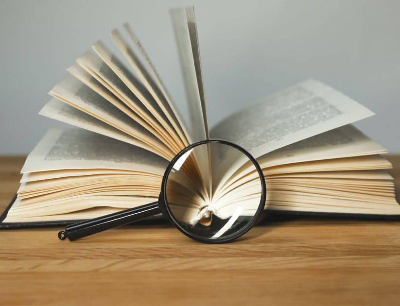 Magnifying glass and open books with turning pages on wood table.
