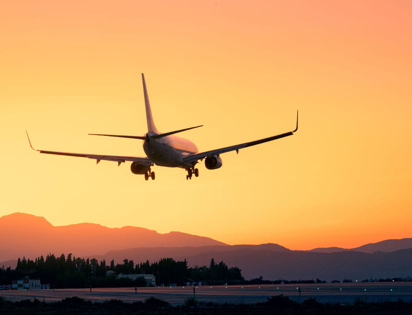 Amidst a breathtaking sunset, an aeroplane lands gracefully with silhouetted mountains in the background