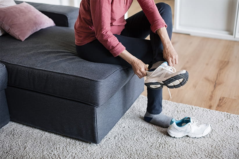 Low section of mature woman wearing sports shoe at home