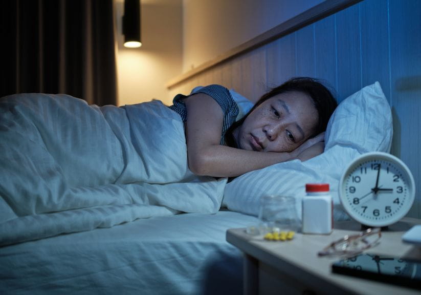 A woman lies on her sleep struggling to sleep, the alarm clock shows 3am