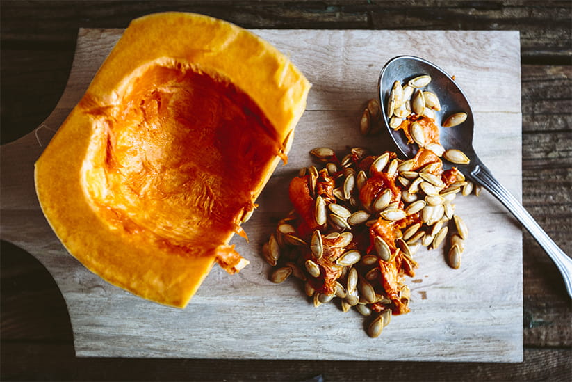 Part of a hollowed-out pumpkin with a spoon and many seeds