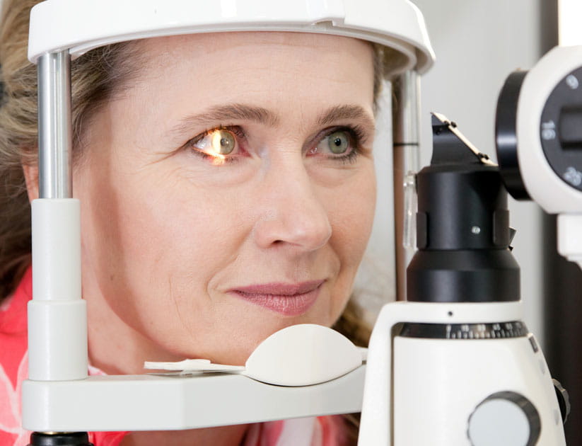 Mature woman at eye exam behind slit lamp, light reflex in eye