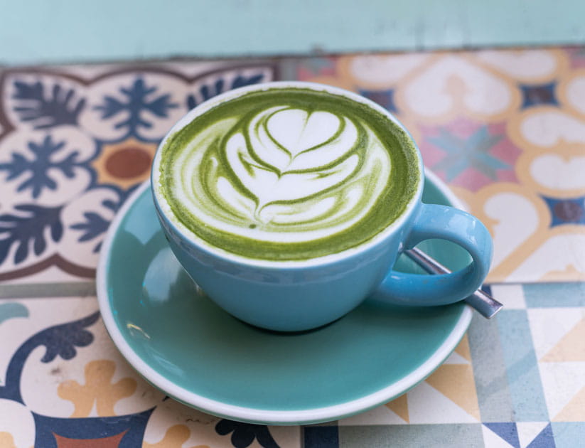 Blue cup with matcha latte with latte art is standing on a colorful tiled tabletop