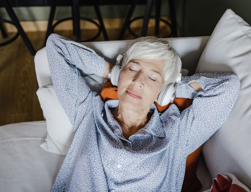 Mature woman relaxing on the sofa with her eyes closed and headphones on