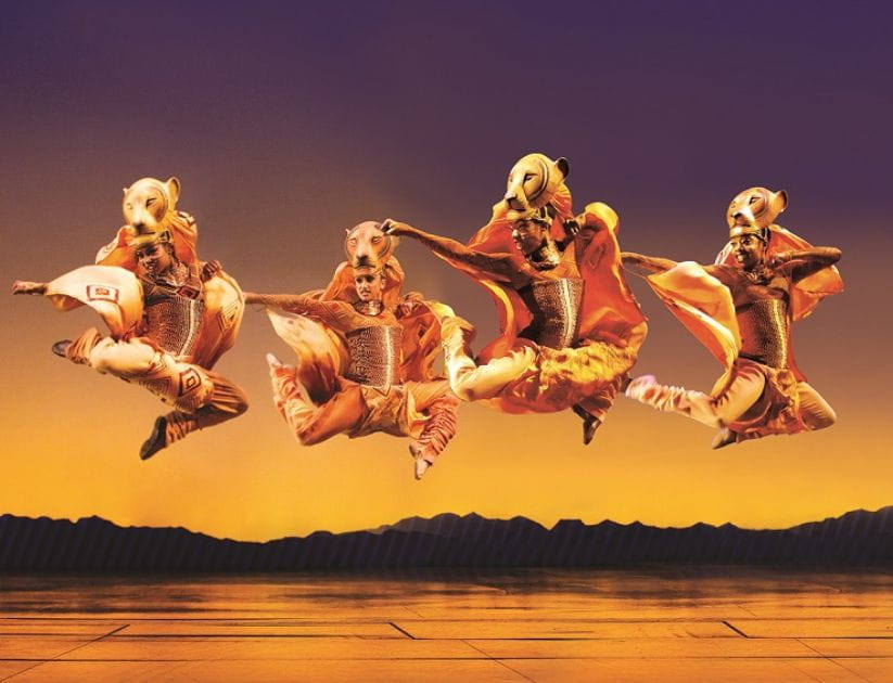 4 actors posed in the air, dressed in lion themed outfits for the Lion King musical