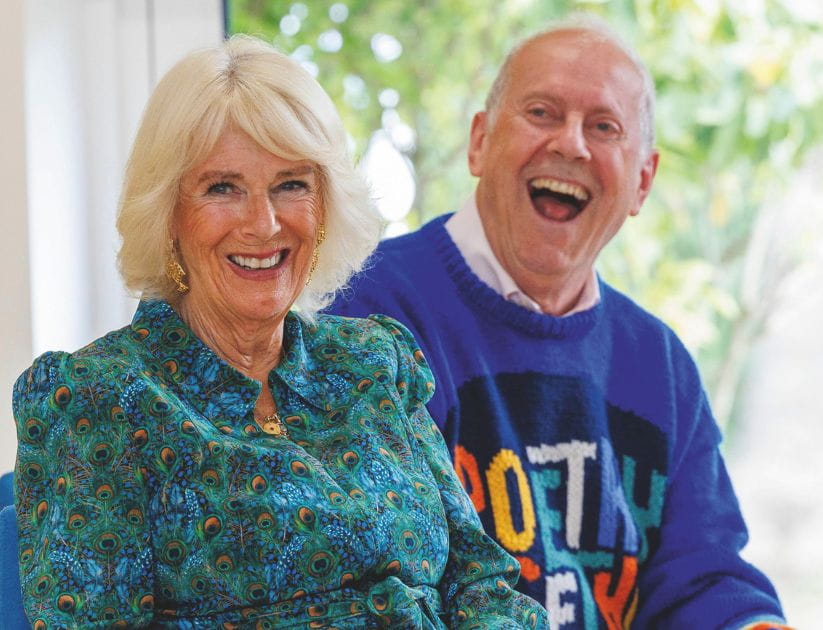 Gyles Brandreth and Queen Camilla sat next to each other smiling  