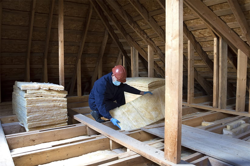 A worker puts glass wool insulation in the attic