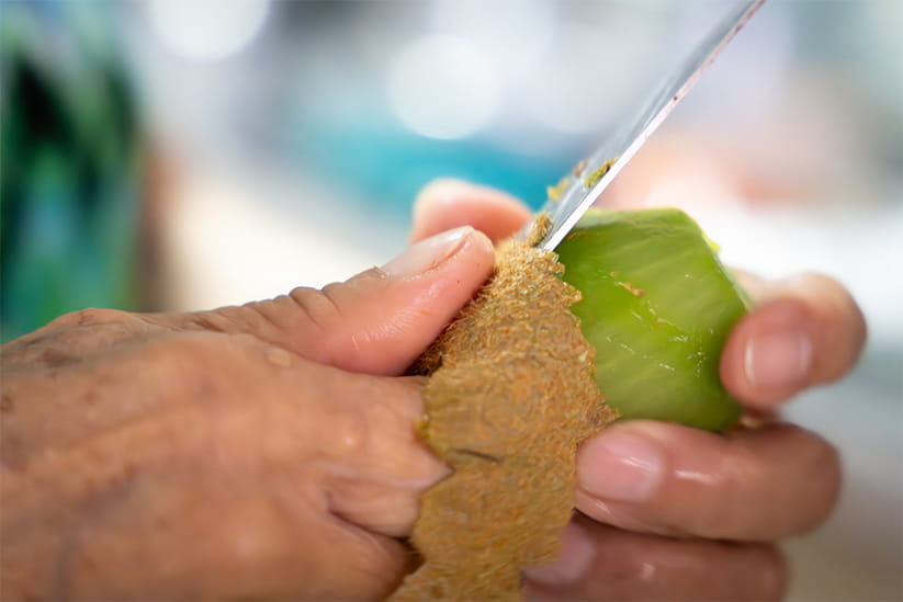 Elderly hands peeling kiwi fruit with a knife in close-up