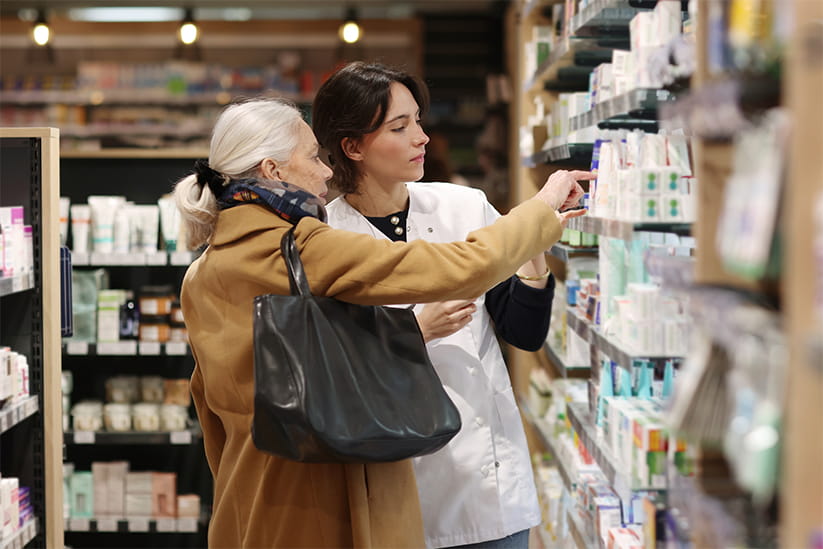A pharmacist recommends products to an elderly woman in the pharmacy aisles