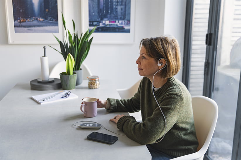 A mature woman uses a medical device for vagus nerve stimulation (neuromodulation) whilst sitting at her dining table